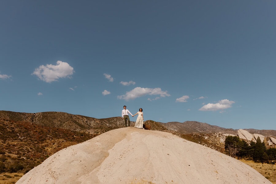 Couple holding hands on top of a sandy hill with a wide view of the mountains and blue sky during a California elopement.