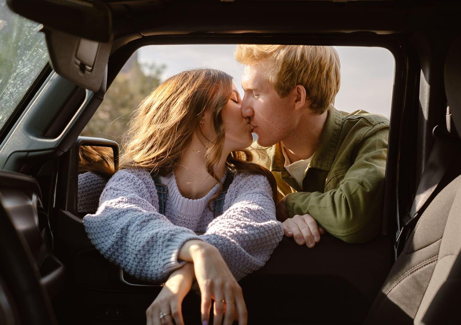 Two people share a kiss inside a vehicle, with natural light illuminating the intimate moment.