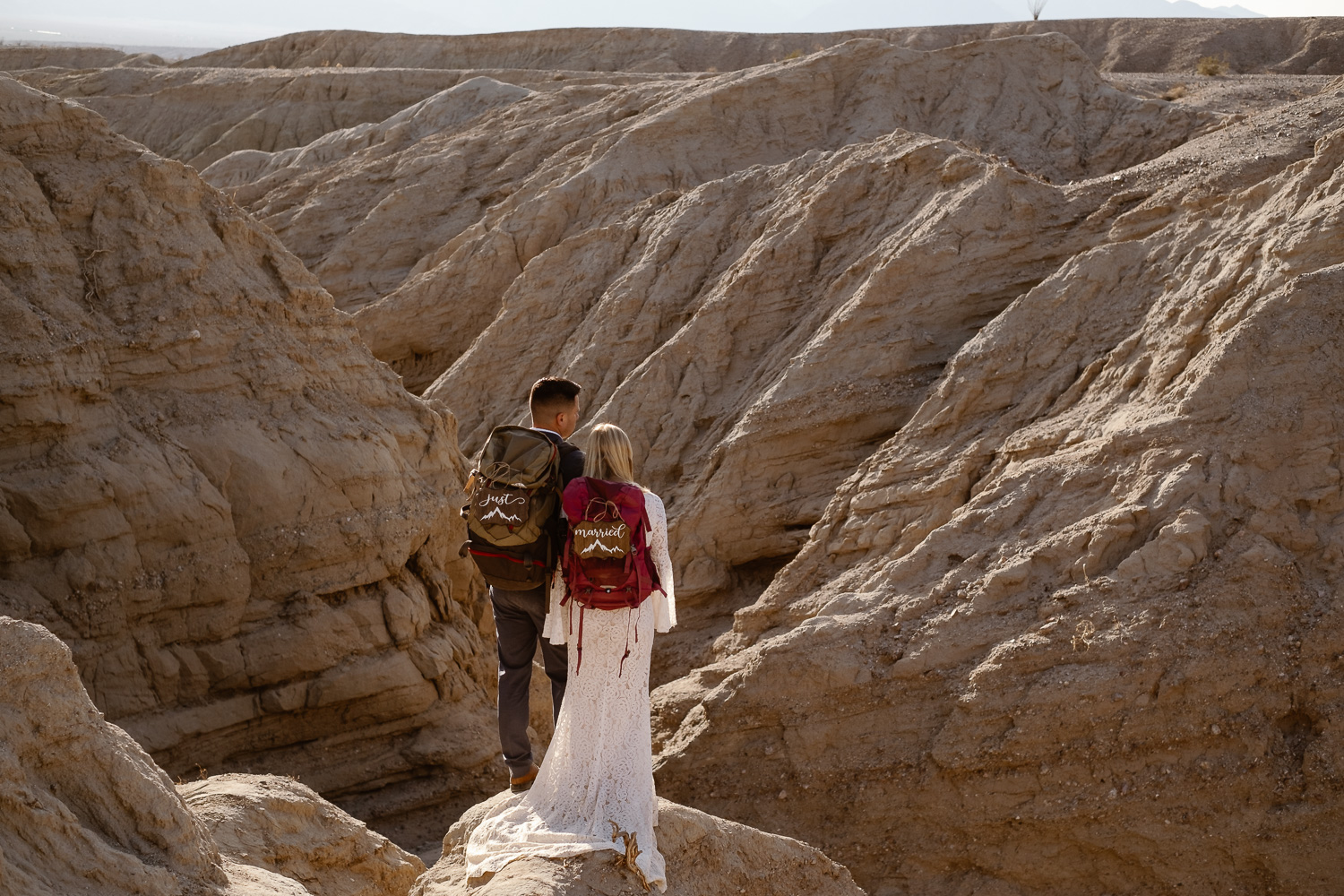 Couple standing with backpacks and wedding attire overlooking canyon.