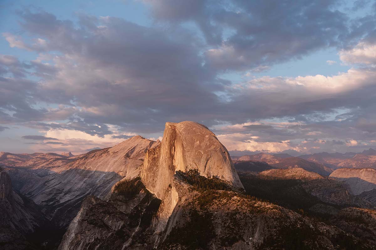 A sunset view of Half Dome in Yosemite National Park with a dramatic sky of clouds and pastel colors.