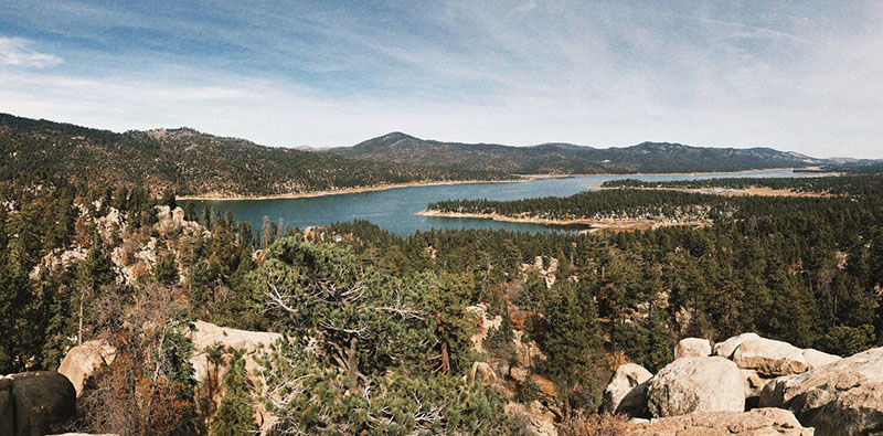 A panoramic view of Big Bear Lake from Castle Rock Trail, showcasing the expansive lake surrounded by mountainous terrain and dense forest.