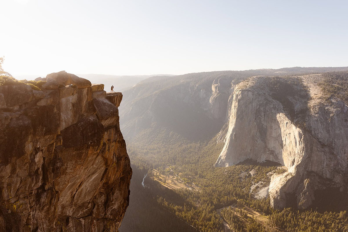 A couple stands on the edge of Taft Point in Yosemite National Park, overlooking the valley and distant granite cliffs.