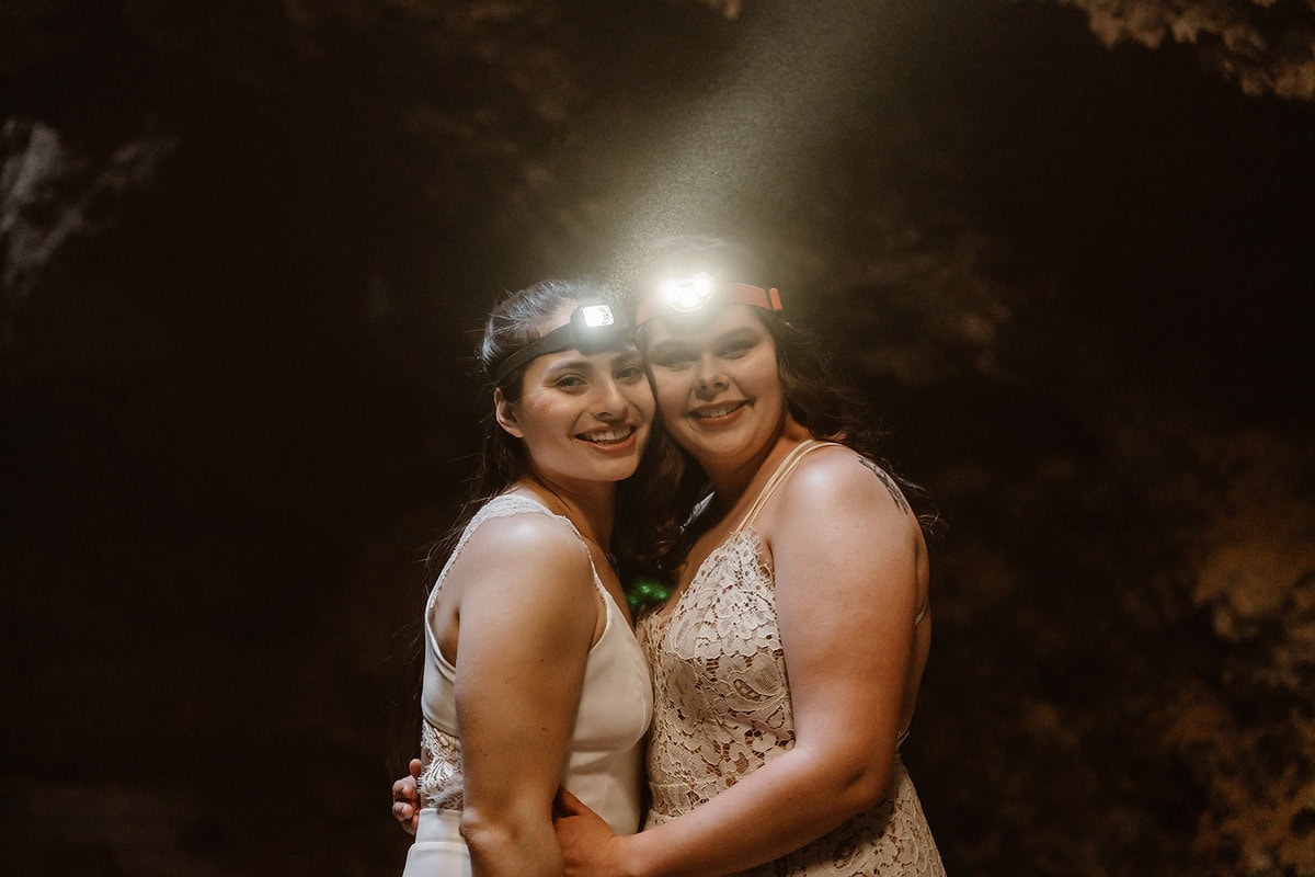 A couple wearing headlamps smiles while embracing inside a dark lava tube during their elopement.