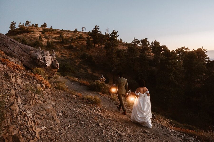 Couple walking uphill with lanterns as the sun sets, wrapping up their California mountain elopement.